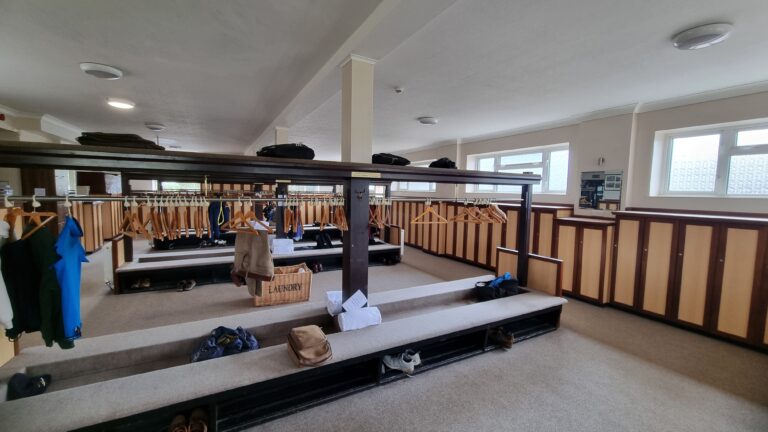 Locker room/dressing area with coats on hangers, benches, and wooden lockers along the walls.