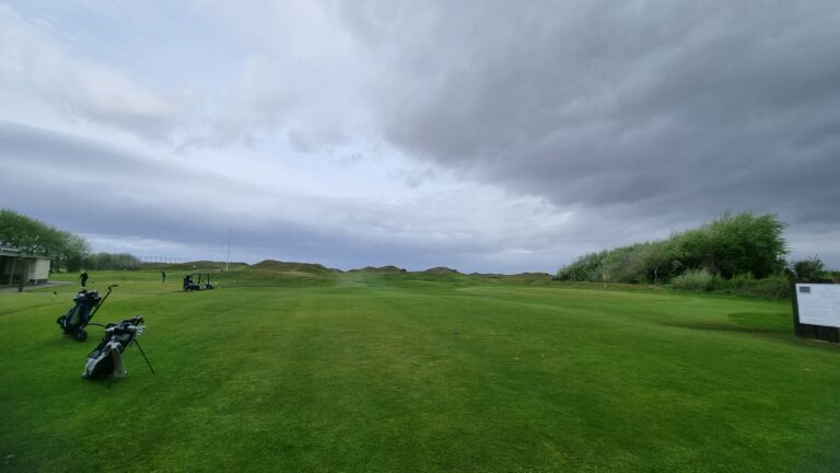 Golf course on an overcast day with green fairways, distant players and golf carts near the edge of the green.