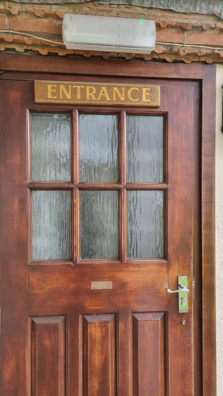 Wooden door with a six-panel glass window and a brass 'ENTRANCE' sign above, set in a brick wall.