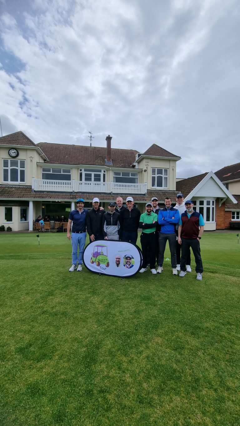 Group of golfers posing on a grassy golf course with a promotional banner in front and a clubhouse behind them.