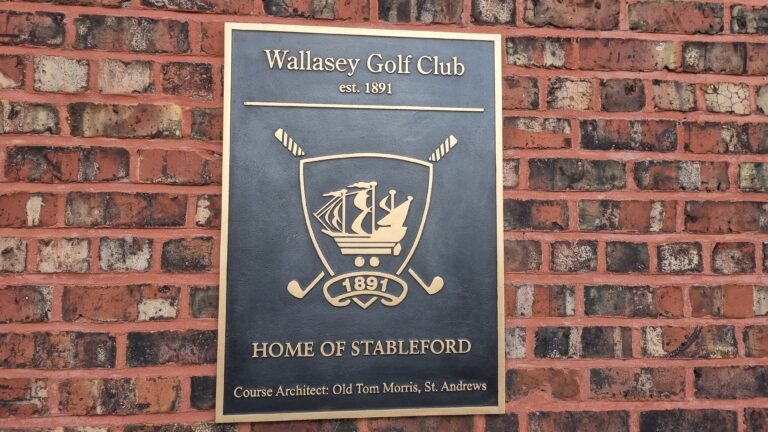 Bronze plaque mounted on a red brick wall reading 'Wallasey Golf Club, est. 1891' with a shield crest showing a ship and crossed golf clubs, and text 'Home of Stableford' below.
