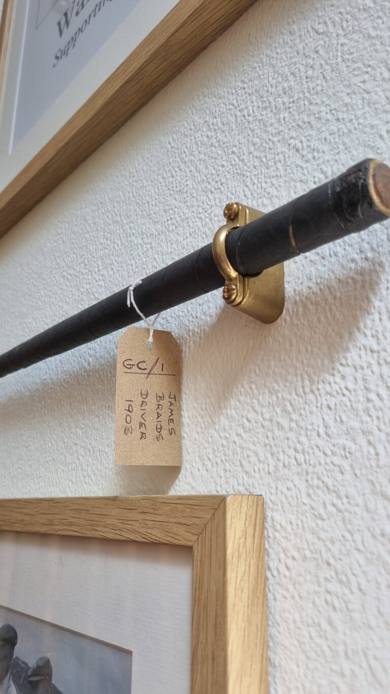 Close-up of a black metal handrail mounted to a textured wall with a brass bracket; a brown tag hangs from the rail with handwritten text.