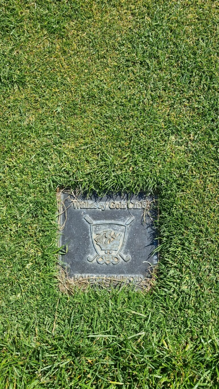 Flat gravestone plaque in a grassy lawn, engraved with Wallasey Golf Club emblem.