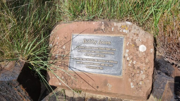 Bronze plaque on a weathered rock reading 'Bobby Jones' with surrounding grass nearby.