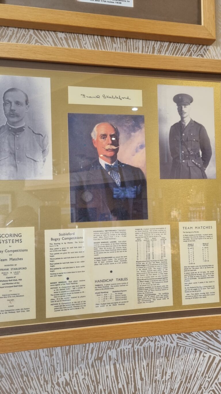Framed display with three portraits: a central color portrait of a mustachioed man in a suit, flanked by two black-and-white military officer photos, plus old score sheets visible below.