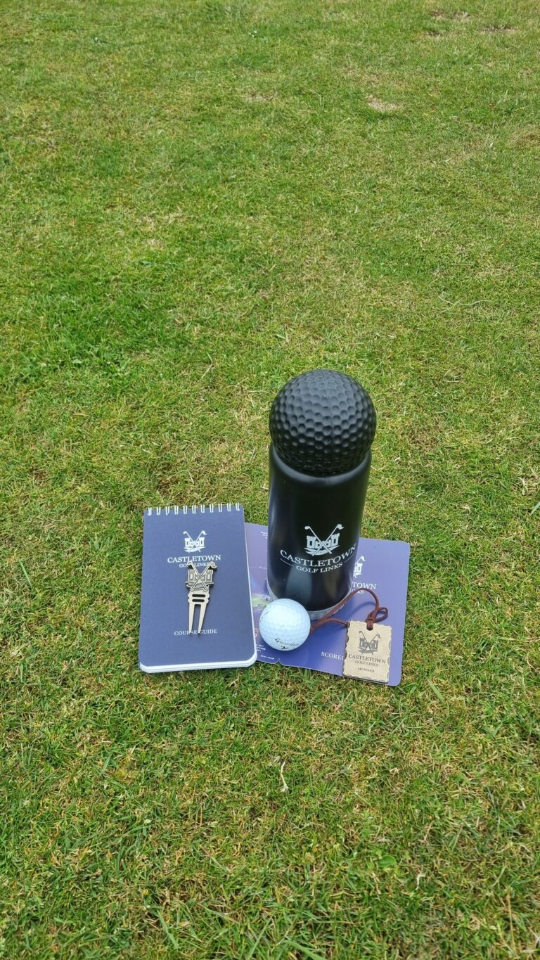 Promotional golf kit on grass: a textured black ball dispenser, notebooks, a golf ball, and event tags.