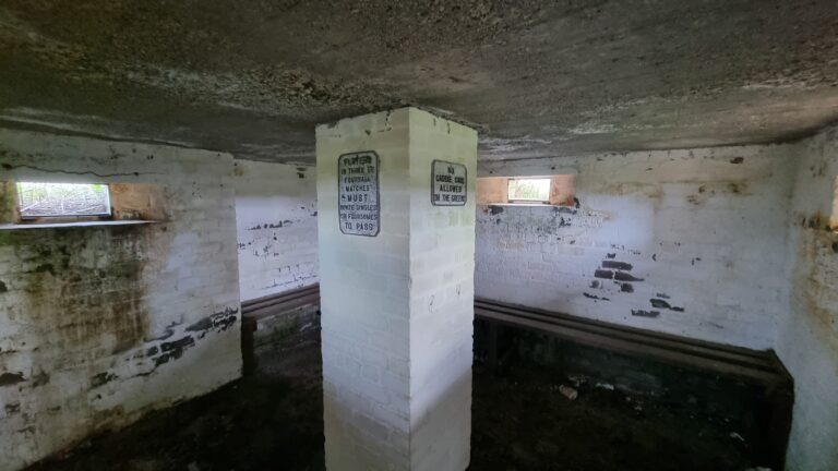 Old, dim basement room with a white brick pillar in the center and weathered walls; signs posted on the pillar hint at game rules.