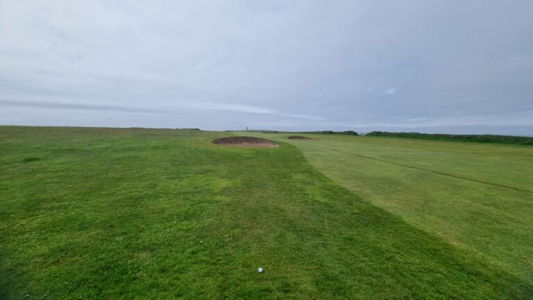 Golf course fairway with two sand bunkers, a ball on the grassy path toward the horizon under a cloudy sky