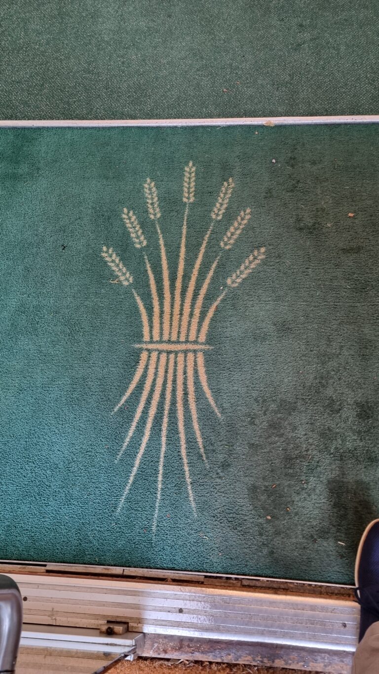 Chalk drawing of a sheaf of wheat tied with a band on a green textured floor surface.