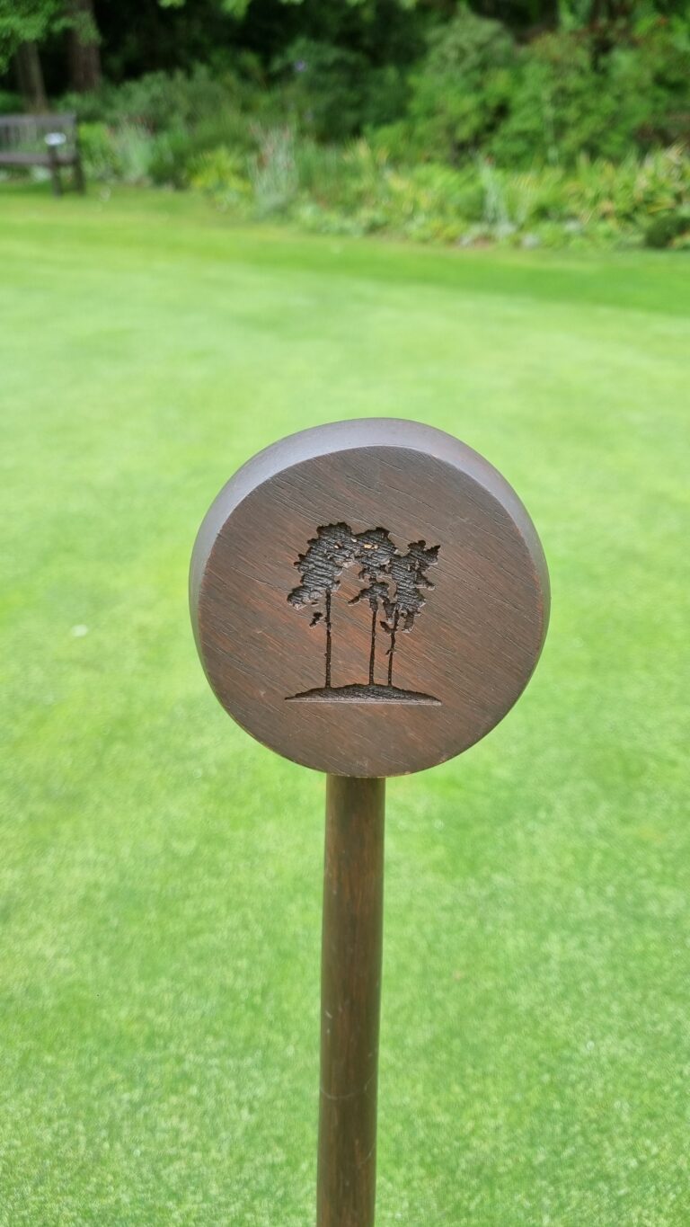 Round wooden plaque with etched palm trees mounted on a post in a green garden lawn